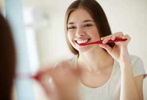 Junge Frau putzt sich vor einem Spiegel die Zähne