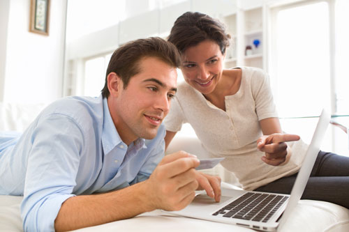 Ein lächelndes Paar sitzt vor einem Laptop, auf dem sie ihm etwas erklärt
